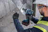 Person i skyddsväst och hjälm använder en blå Bosch borrmaskin på metall.