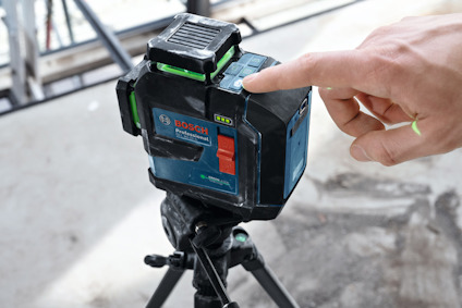 Laseravståndsmätare från Bosch på ett stativ, med en hand som justerar inställningarna på enheten.