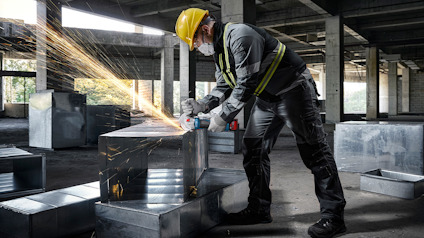 Arbetare i skyddsutrustning slipar metall i en industriell miljö, gnistor flyger från materialet.