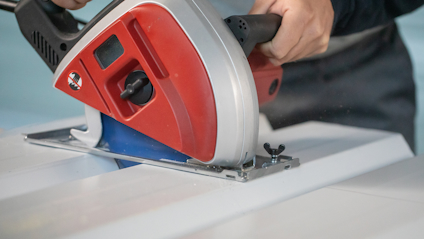 Person använder en röd och silverfärgad elektrisk cirkelsåg för att skära en vit panel.