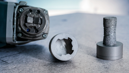 Metallverktyg nära cylindrisk del med grövre yta på grå arbetsyta.