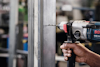 En person använder en Bosch borrmaskin för att borra i en metallram, med suddig bakgrund.