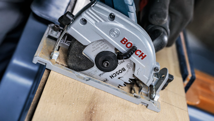 Cirkelsåg från Bosch skär genom trä, hålls av en person i svarta handskar.