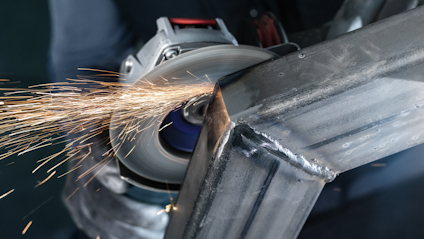 Hörn av metallkonstruktion svetsas av arbetare med vinkelslip, gnistor flyger.