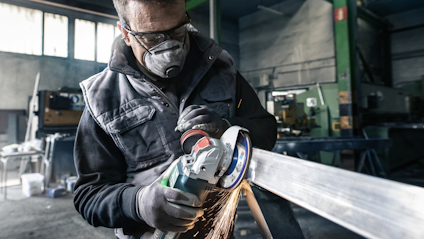 Person med skyddsglasögon och mask slipar metallstång, gnistor flyger åt sidan.