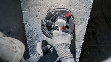 Person i grå handskar slipar betong med en elektrisk slipmaskin.