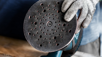 Rund slipmaskin med perforerad slipplatta, hålls av handskbeklädd hand.