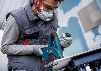 Person med skyddsglasögon och mask använder en Bosch elektrisk verktyg.