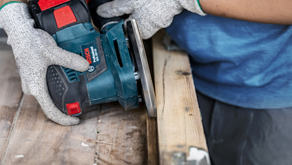 Person med skyddshandskar slipar träplanka med Bosch bandslipmaskin.