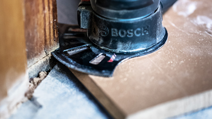 Bosch-verktyg kapar en träplanka nära en dörrkarm inomhus.