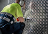 Person i skyddsutrustning borrar i en mönstrad metallplåt.