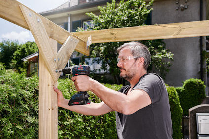 En person borrar i en träkonstruktion utomhus med en sladdlös borrmaskin.