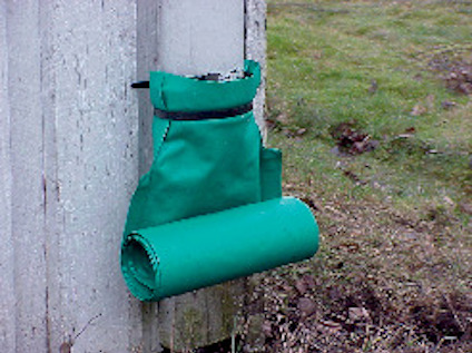 Grön rulle i plastficka fäst på en vit vägg utomhus, gräs i bakgrunden.