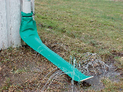 Grönt avloppsrör från stuprör leder vatten som sprutar ut på gräsmattan.