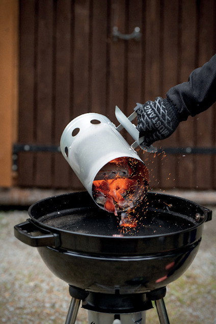 Kol hälls från en tändrörsstarter ner i en klotgrill av en person med grillvante.