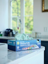 Kartong med "Universal Cleaning Cloths" på köksbänk, gröna trasor synliga.