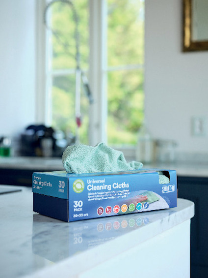 Kartong med "Universal Cleaning Cloths" på köksbänk, gröna trasor synliga.