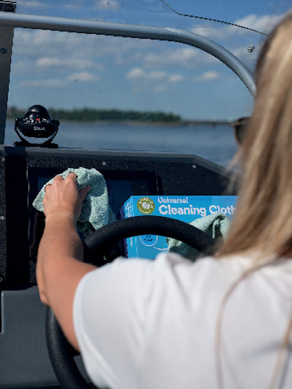 Person torkar av en båtstyrpanel med en grön duk, en blå förpackning med texten "Universal Cleaning Cloth" syns.